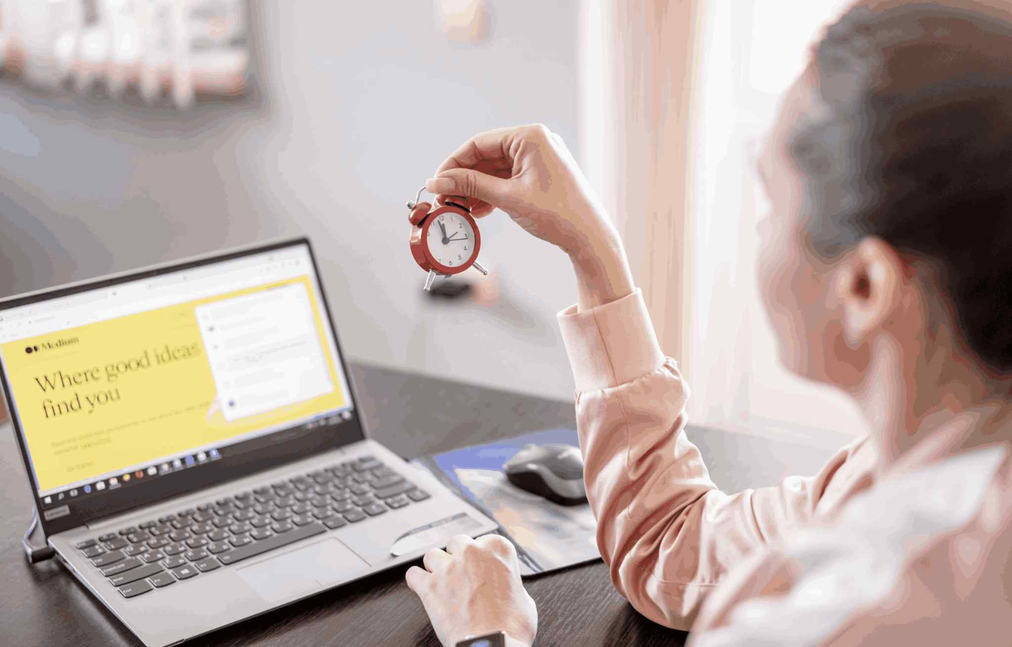 Person holding a red alarm clock while working on laptop